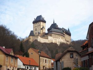 a typical fairytale castle: with a tower and defensive crenellations on its walls, perched high on a hill above the village visible in the foreground: Visiting Karlstejn Castle from Prague