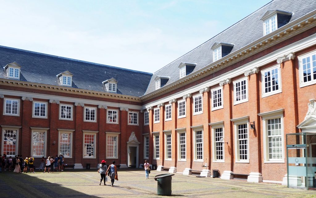 This photo shows two sides of the courtyard: two story buildings with a further story under the roof. The walls are simple red brick with columns, also brick, between the windows. 