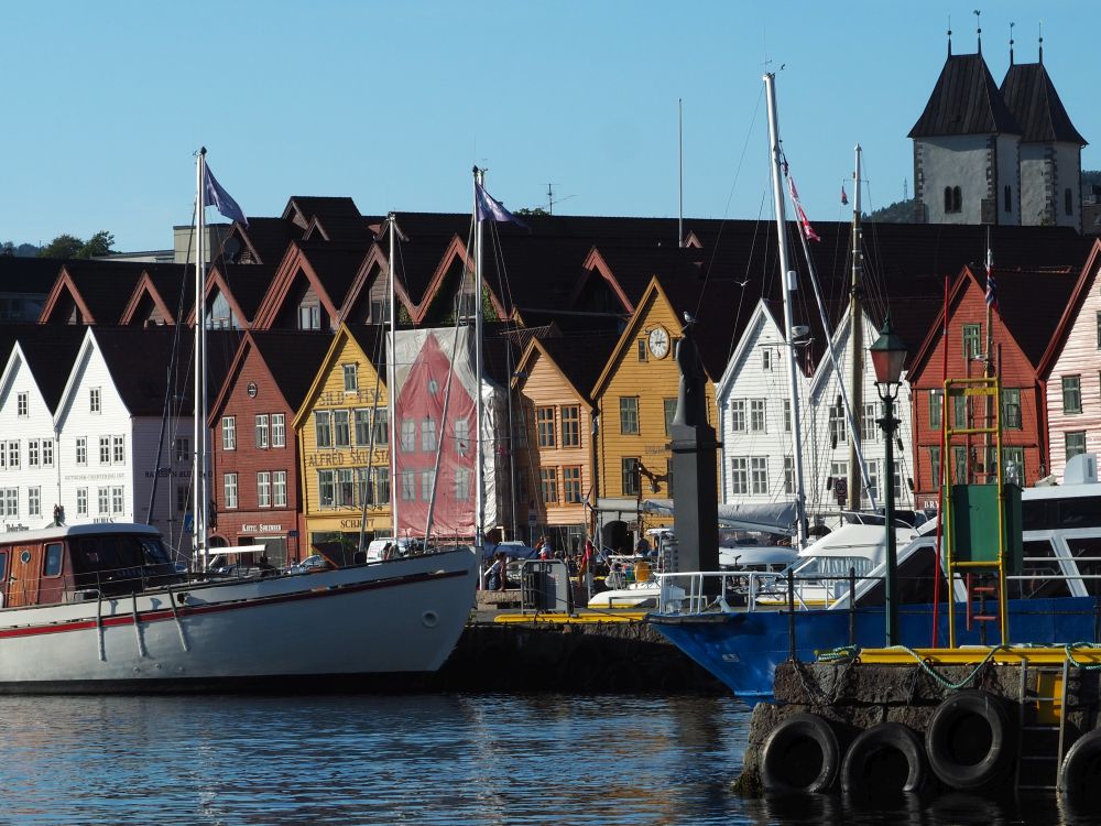 A row of houses all adjoining each other, painted in a range of colors. In front of them, several boats are moored.