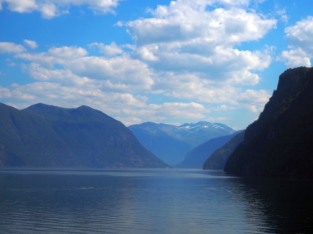 rocky, steep mountains on either side, dropping straight down into the water in the center. In the distance, a higher mountain, with a bit of snow visible on top.