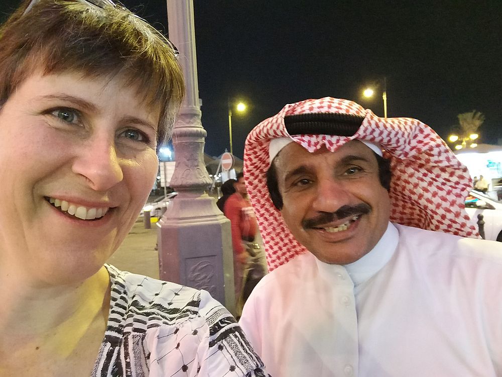 A picture of Rachel with Naawaf Al Shammari, a famous Kuwaiti actor, in the Kuwait market. He is wearing a traditional red and white headdress.