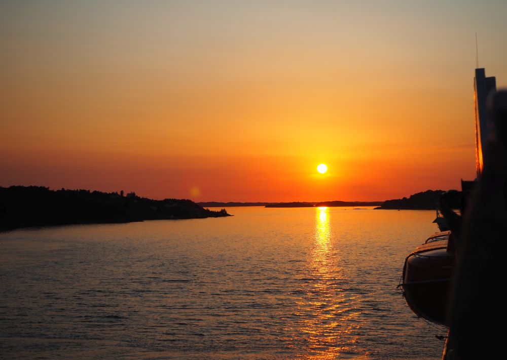 A very orange sky with a bright orange sun in the middle of the picture, and an orange stream of light on the water. Hurtigruten review.