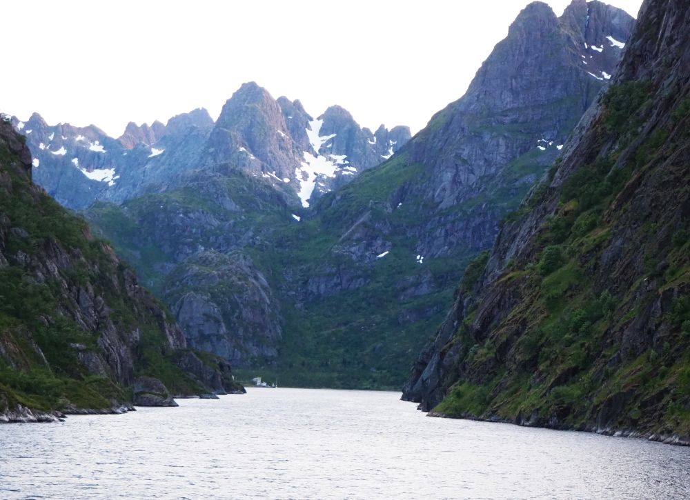 A small opening shows between two steep cliffs on either side. In the background, more steep cliffs, some showing snow in the clefts.