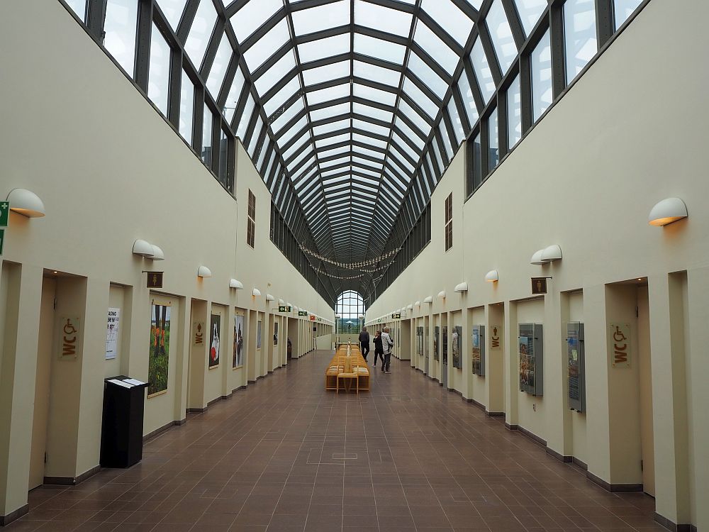 Among the things to do in Rovaniemi is to visit Arktikum. Ahead is a long, straight hallway with doors lining both sides. Above, the second story is an arched glass roof, the whole length of the hall. At the very end, far in the distance, a glass window is visible.