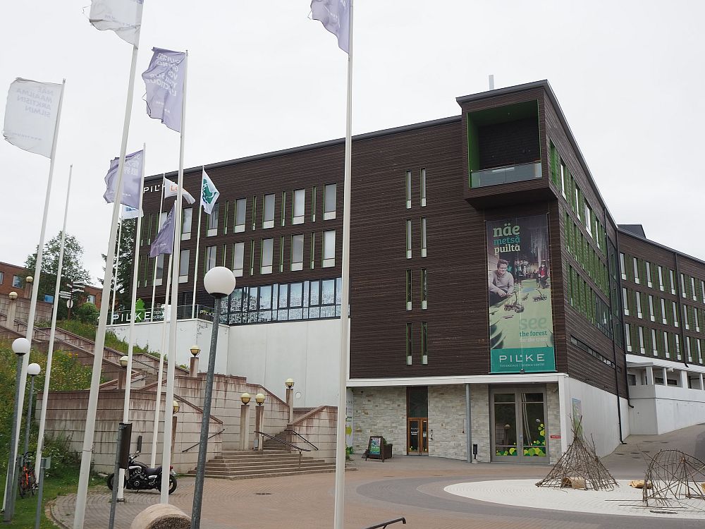 Among the things to do in Rovaniemi is to visit Pilke science center. The building is large and modern and partly built into a hill on the left. The bottom story is white, while the 4 floors above are dark brown. A piece of the top floor extends out over the entrance: a little porch, I think. 