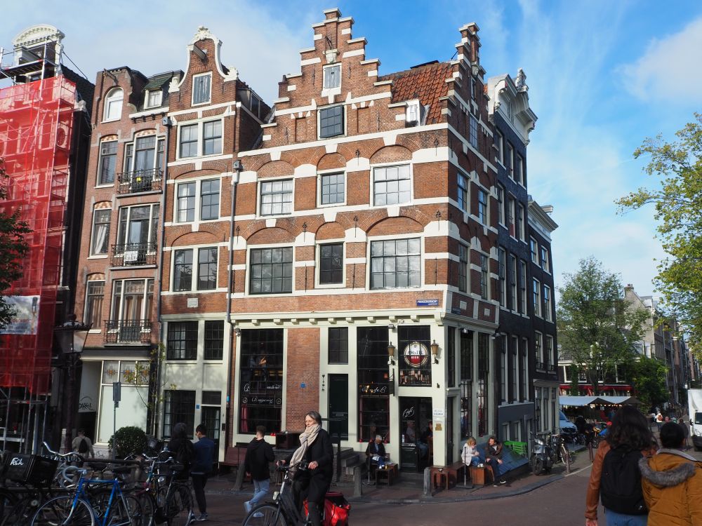 A pretty corner building, 4 stories high, red brick with white details and a pretty stepped gable. 