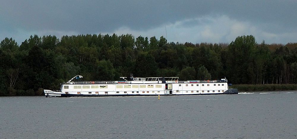 De Nassau, our Boat Bike Tours ship. The water is wide here, and the ship - long and low and riding low in the water - is closer to the far bank, which is forested.