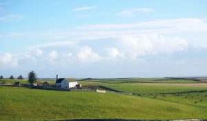 a green, grassy, rolling hills landscape with, on the left, a small church with a wall around the churchyard.