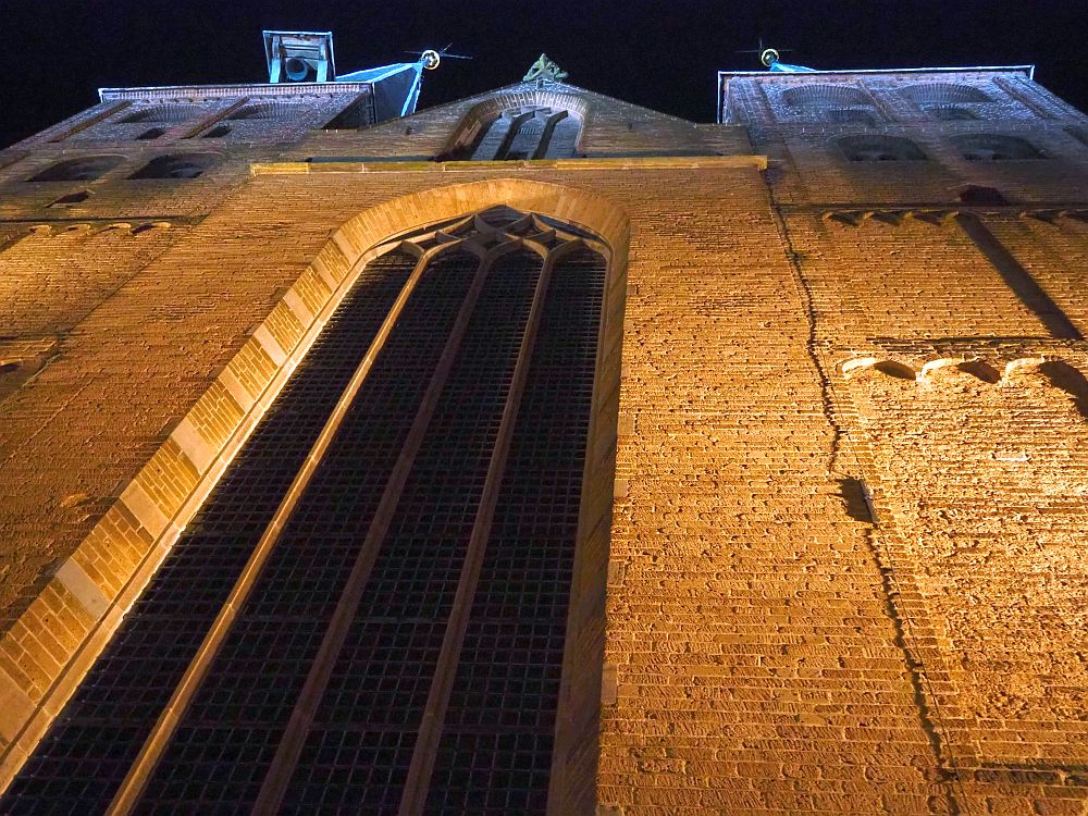 A night view looking straight up the church front: red brick with a tall, gothic window up the center and a peaked roof.