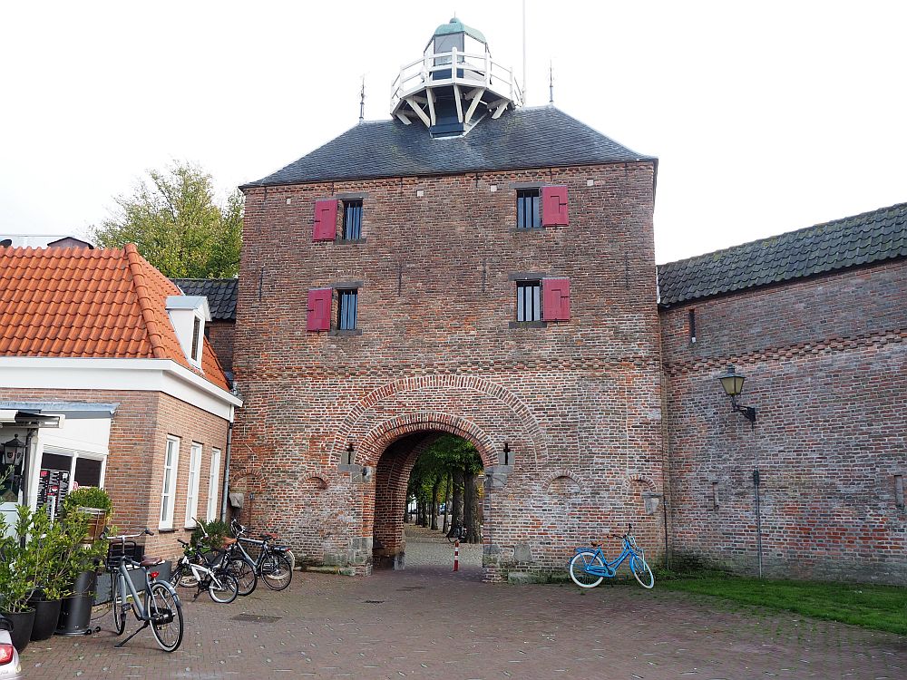 The building is square red brick, with a arched opening through the ground floor and two windows for each of two floors above it. On the top a small round thing protrudes with a round balcony around it: the lighthouse.