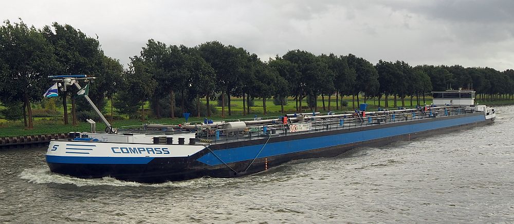 The boat shown is very low to the water and is seen from near the front. The bow is on the left of the picture and the stern in the distance on the right of the picture. It looks like a tanker; lots of piping is visible in the center of the boat.