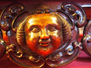 a carved, wooden face glows golden. It is round and smiling, with tight curls on either side. 