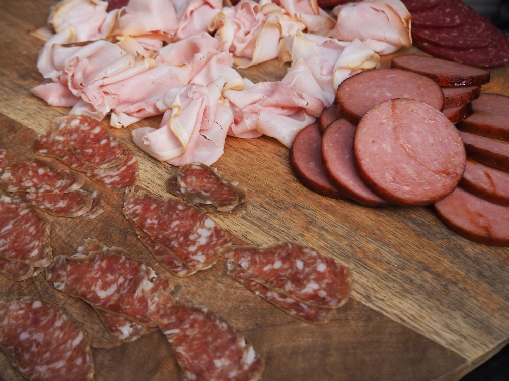 ON a wooden board, slices of salami, smoked ham and round slices of some sort of bologna.