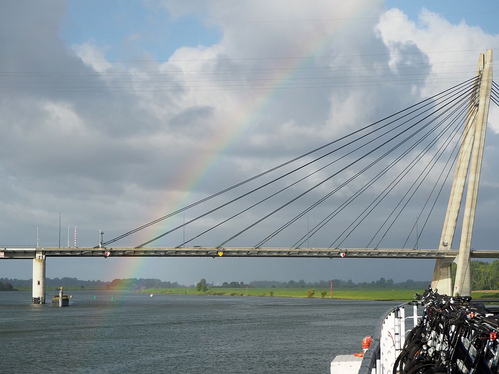 Part of a suspension bridge crosses the picture, with a rainbow visible against the clouds.