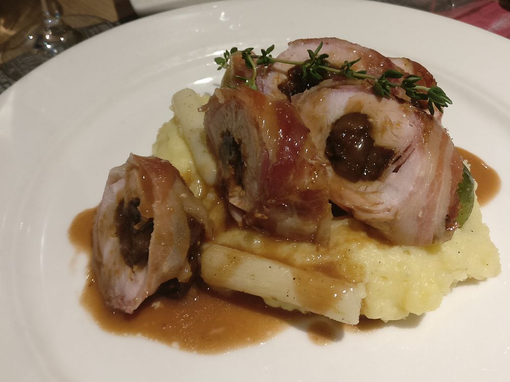 Slices of roulade on a bed of mashed potatoes, with a sprig of thyme on top and dribbled with brown gravy.