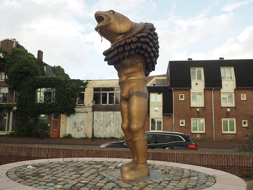 The statue has a human man's body but has no arms and the head is the face of a fish, while it wears a large bumpy ring around its shoulders.