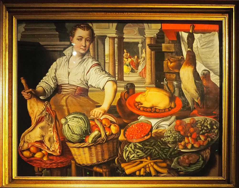 In the foreground of the painting is a woman hoding a leg of lamb and a basket of fruit and vegetables. Behind is a gateway with columns and beyond that is a cluster of several people.  