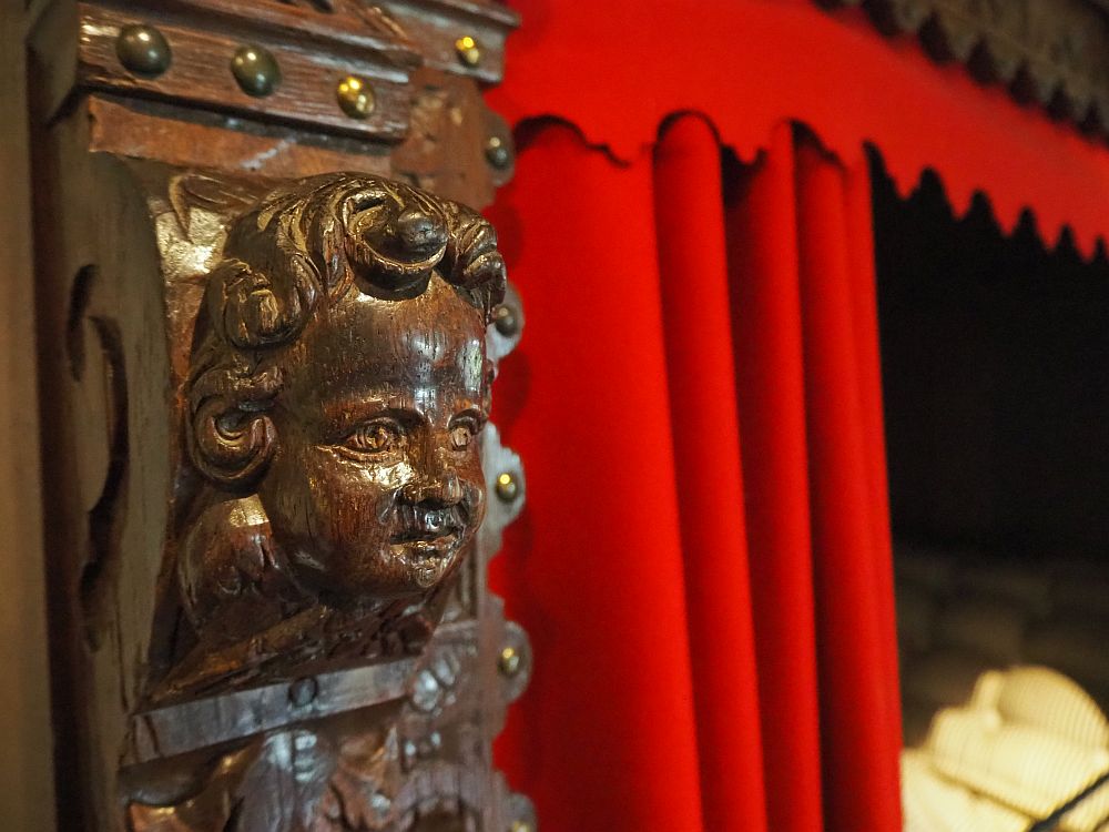 A dark wood carved cherub's face. Behind that, a red curtain.