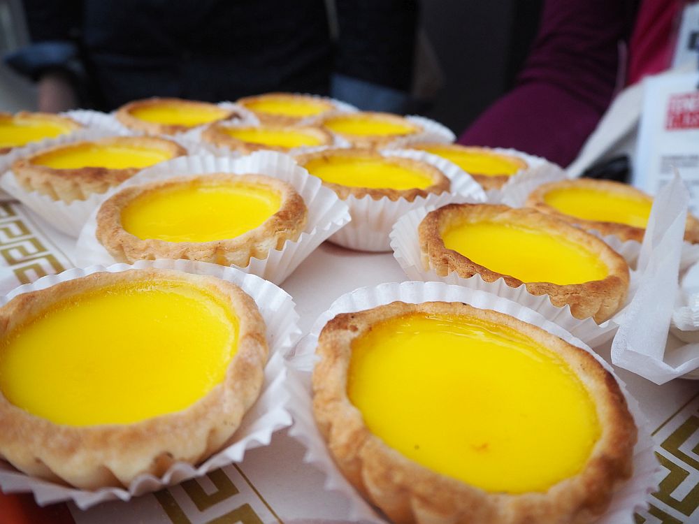 a tray of custard tarts: fluted pastry edges and bright yellow centers, each in a pleated white paper cup. Taken on one of the Tenement Museum tours.