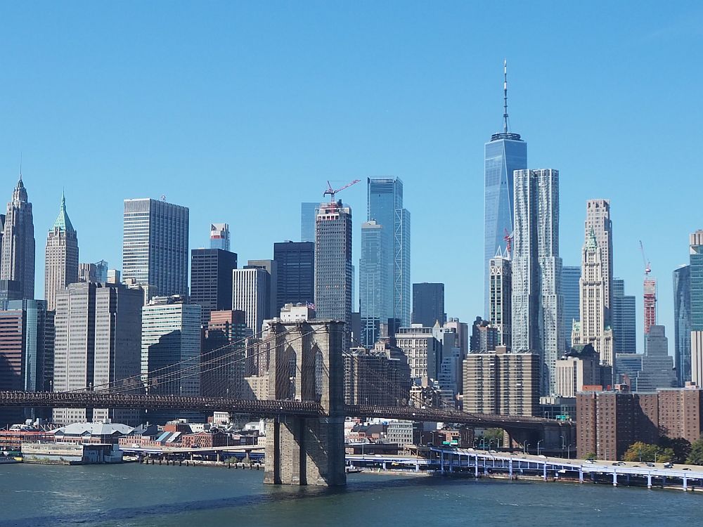 A cluster of skyscrapers with one pier of the Brooklyn bridge in the foreground.