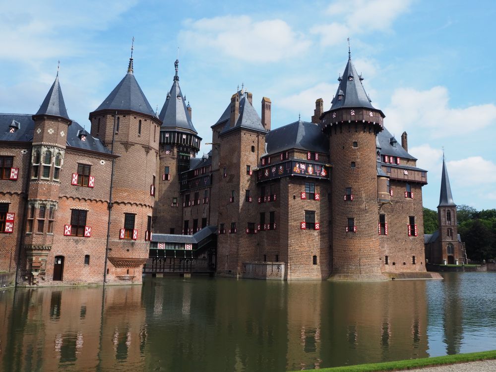 This view of Castle de Haar has about 5 turrets, not counting smalller decorative ones. Here the castle appears to rise from the water of the moat. On the right, just visible beyond the castle, is a small church with a spire in front.