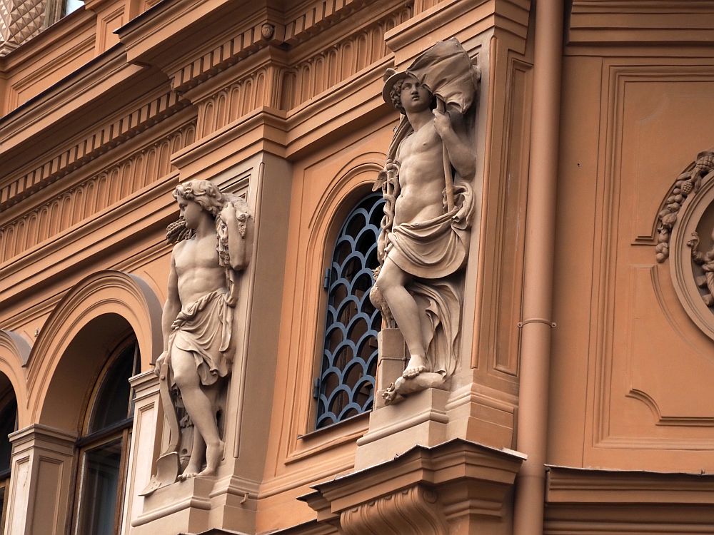 Between arched windows are two classical-style statues, both of muscular young men, naked except for draped cloths around their waists. 