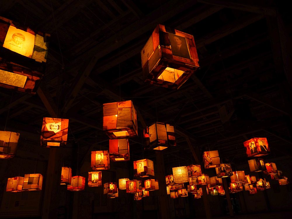 Against a black background are lit-up square lanterns, perhaps 30 or so, and pictures of people are visible on each one.