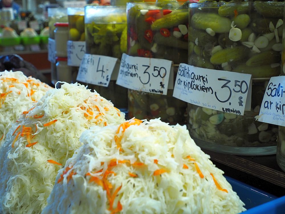 Foreground: piles of cole slaw.
Background: big jars of pickles with price labels on them.