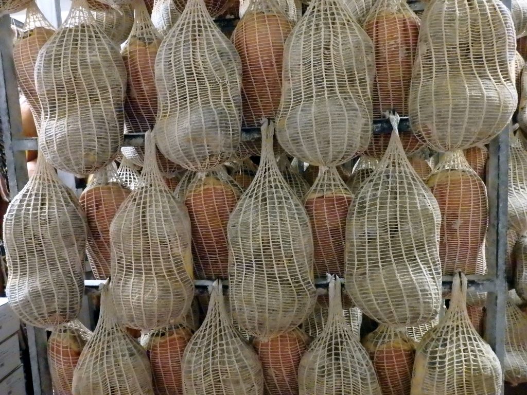 Parma hams in net bags hanging to dry on a rack. 