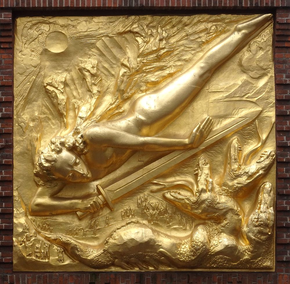 The bas-relief portrays a figure of a human angled from top right to bottom left, head downward. He/she holds a very long sword, pointing to top right. Some sort of creatures, perhaps dragons, are lower right. The whole thing is shiny gold.