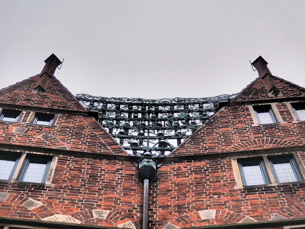 Two pointed top strories of a building. Between them are horizontal bars, from which the small bells hang.