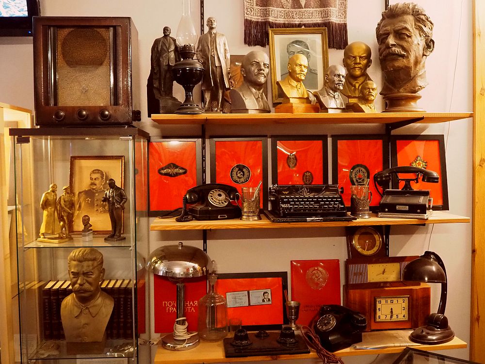 Shelving on the right, a glass case on the left. The shelves hold a variety of items: an old radio, several old telephones, a typewriter, several lamps, a collection of heads of Lenin and Stalin, some framed items that I think are medals, some clocks, etc. It's hard to see if any of this had anything to do with communism in Prague, or whether they were just Russian bric-a-brac.