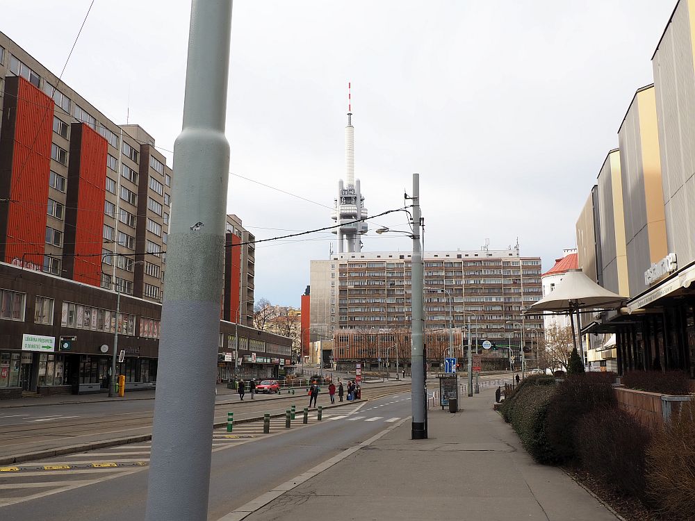 Looking down a wide street. On the left is a concrete building with windows in rows on each story. It has vertical red blocks here and there - perhaps elevators added later? On the right it's hard to see if the building has windows at all. The building straight ahead is another concrete one: apartments, probably. Beyond that is the tower, much taller, with  "pods" protruding from it about halfway up.