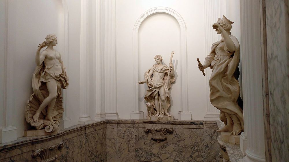 Three classical stone statues perch on a ledge in the Willet-Holthuysen Museum against 3 white-painted walls. On the left, a woman (Venus?) standing on a seashell, her breasts exposed, cloth draped around her waist. Straight ahead, a man, also exposing his middle, with cloth draped around his neck and his waist but, like the Venus, with his legs exposed. A dog peeks from behind his legs. On the right, another similar woman, but wearing a crown and holding what looks to be a flute. 