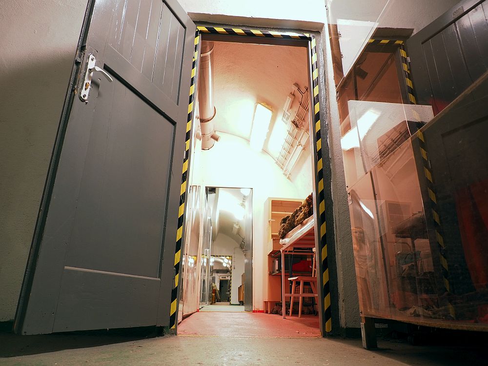 Photo taken from floor height looks through an open doorway. The first visible room seems to have a bunk in it, a chair and some shelves. Several doorways into the distance are visible straight ahead, but not what's in each room.