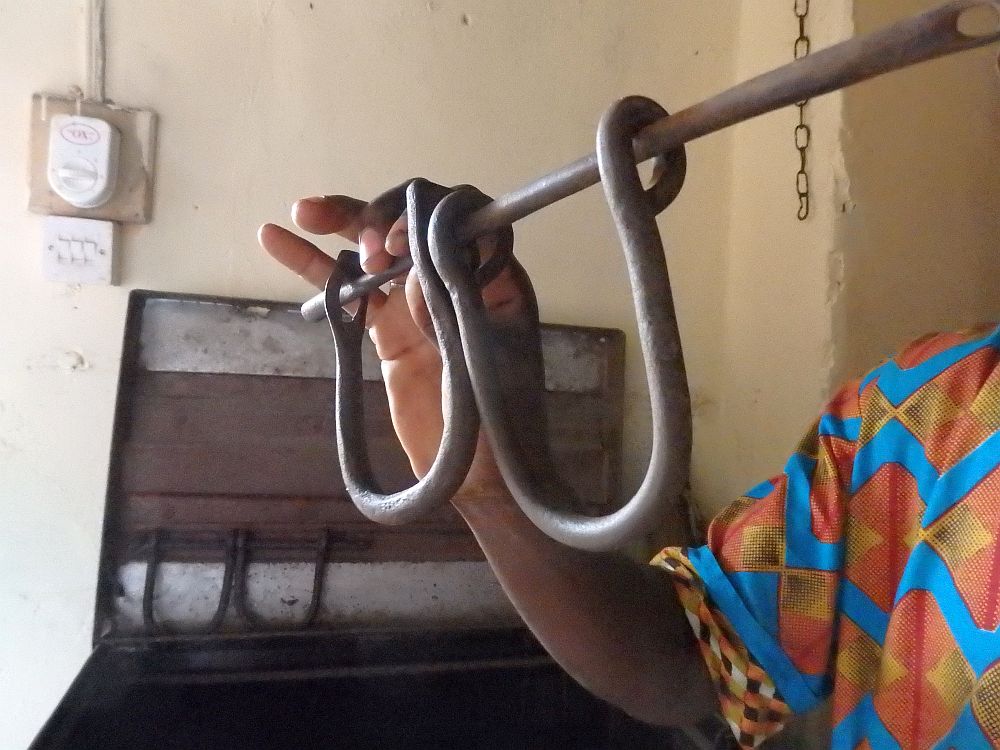 Our Badagry guide holding up a set of leg irons. It consists of one horizontal metal bar and two more, each bent into a U shape and hanging from the straight bar.