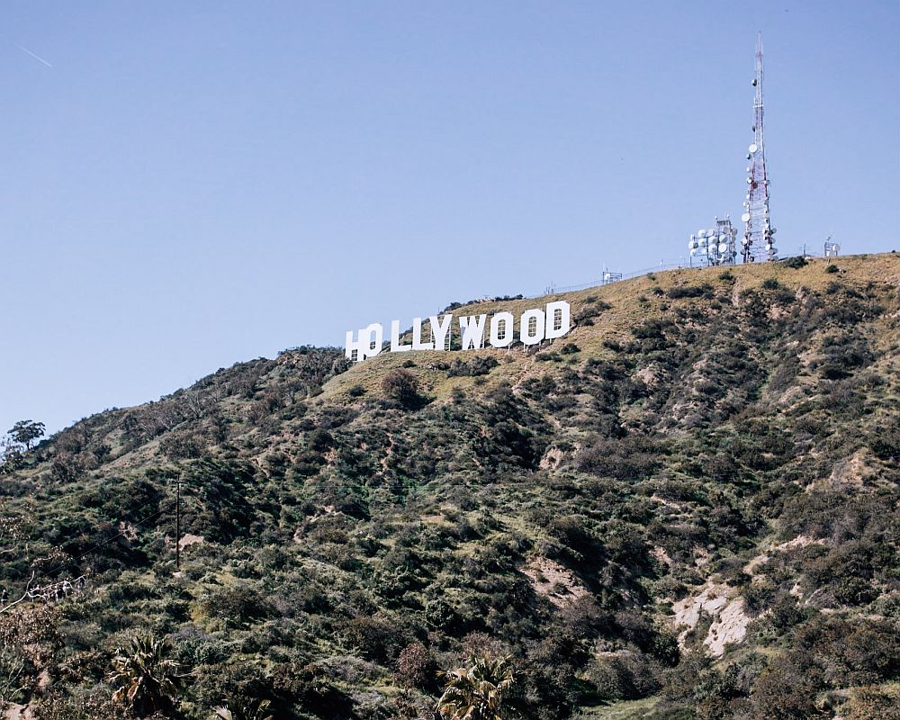 The famous Hollywood sign, near the top of a brown hill covered in scrub. Near the letters, right on the top of the hill, is an array of satellite dishes, some on a tall tower, some clustered on a lower structure.