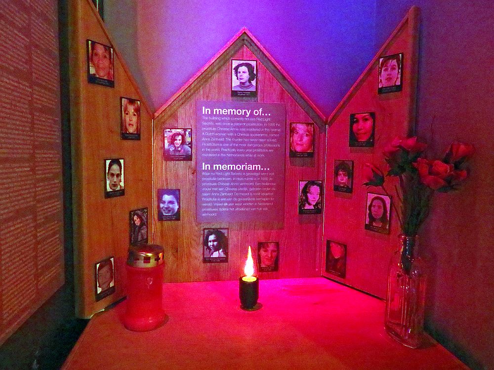 The small altar is simple wood, with 16 small pictures of women on it and a sign in the middle that says "In memory" and explains the purpose of the memorial. A candle burns in the center in front of it and a bunch of flowers stand in a vase to the right.