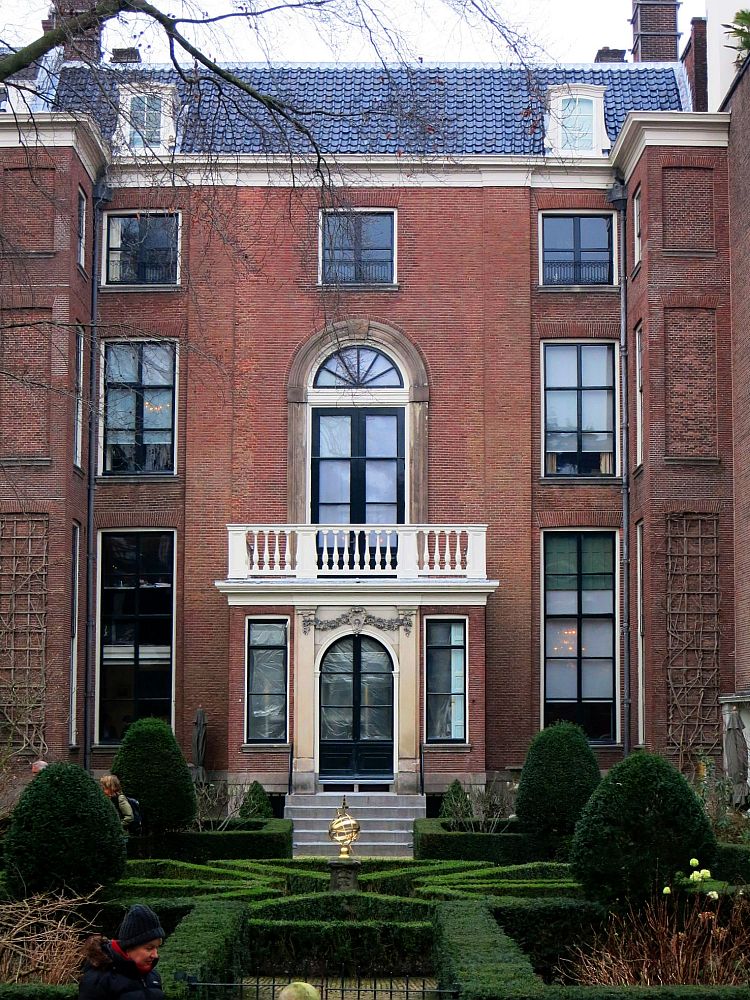 Elegant, symmetrical red-brick building with 3-4 stories. Neatly trimmed shrubbery in the garden.