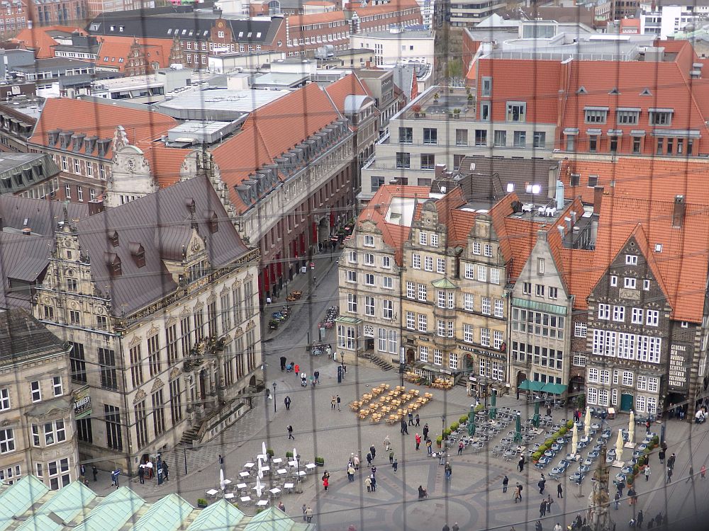 Looking down on an open square, with a row of historical buildings on one side, each with a stepped or pointed gable and many windows. 