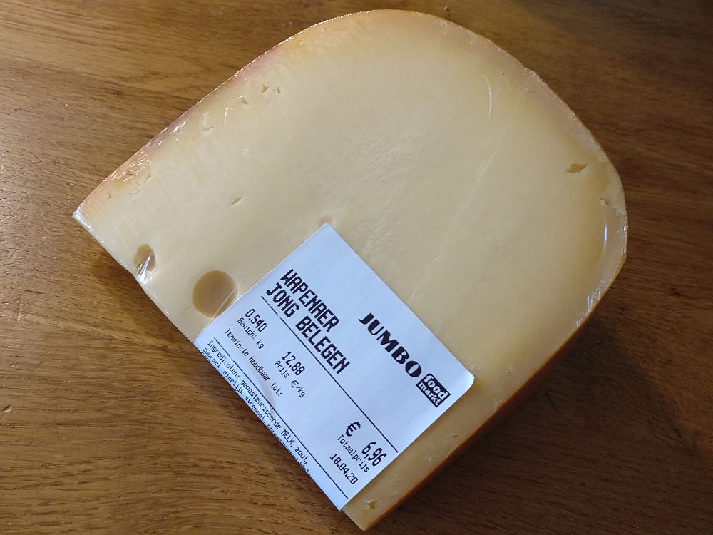 A wedge of cheese wrapped in plastic with a supermarket label, translated: Jumbo food market, Wapenaer Jong Belegen, weight 0.540 kg, price in euro/kg 12.88, total price 6.96. 