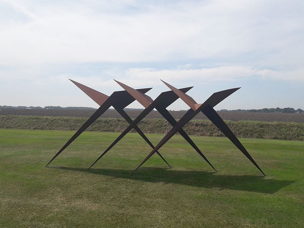 In an open field, the sculpture is made of flat pieces of iron in the shape of three X's.