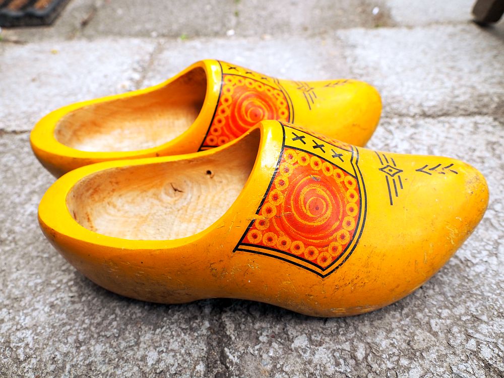 A pair of typical Dutch clogs, painted for the tourist market. They are made of wood but painted on the outside in yellow, with a decorative pattern on the front from the top edge to the toe: red circles on each side, xxx down the middle in black, and a few simple lines on the toe.