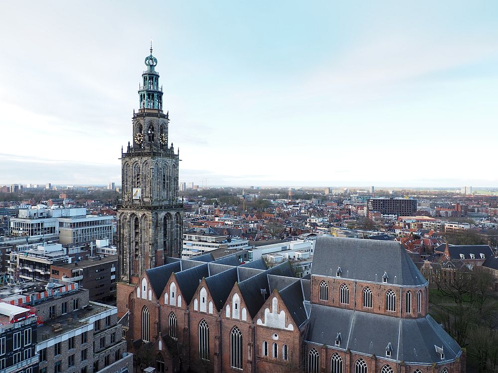 Looking slightly down at the Martinikerk (St. Martin's church) with the Martinitoren at its front. The church has gothic arches but no buttresses. The tower is red brick at the bottom (matching the church) and grey stone above. It has gothic arches too, in several levels, like a very tall, narrow wedding cake. At the top is a green (copper, I assume) tower top, with a round bulb shape at the top.