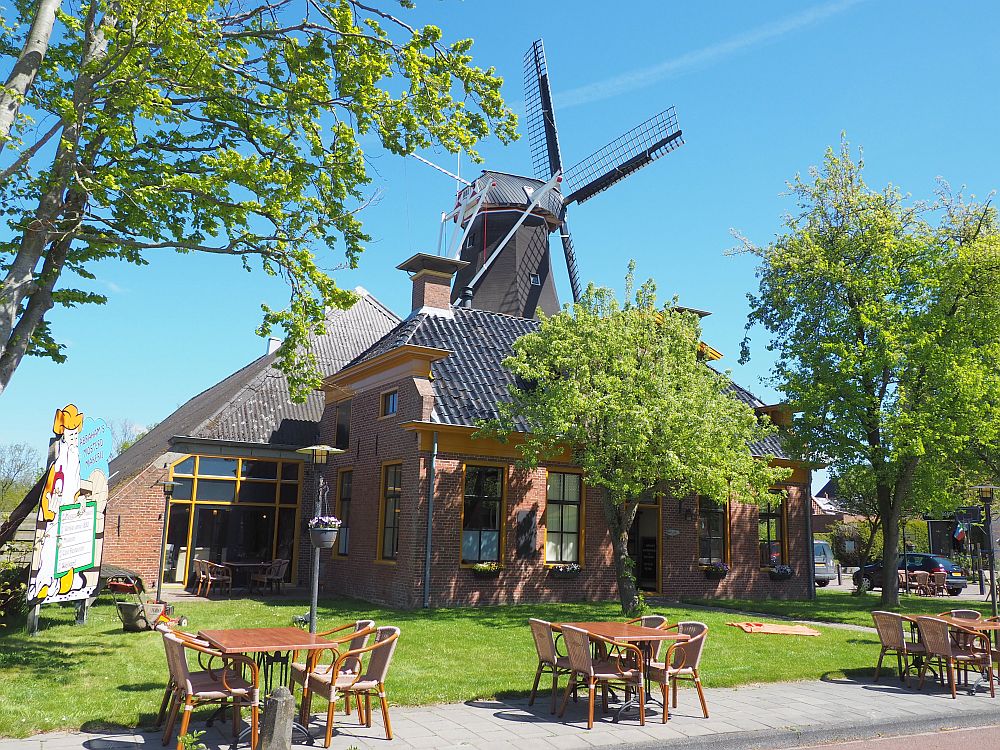 The mustard factory looks like a typical Groningen farmhouse: red brick with a much bigger barn behind and attached to it. Behind that a windmill (De Lelie) Is partially visible: just the top and the vanes.