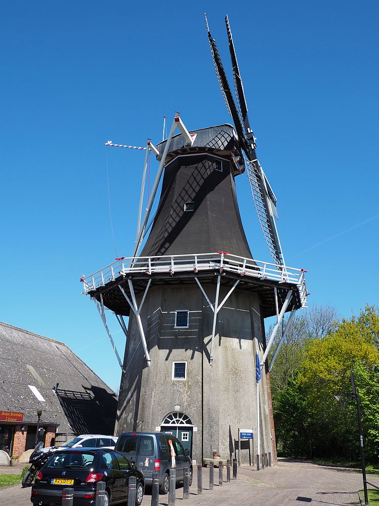 The windmill is quite tall: A door is visible at the base, with two small windows above it indicating two additional stories above it. Above that is the "balcony" all around the mill, which appears to be six or eight-sided. Above that, it's about the same height as below the balcony, making the total height about 6 stories. This is a side view, so the vanes are on the right. 