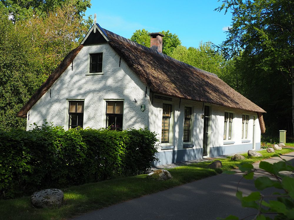 The house is brick, but painted white with a thatched roof. It seems to be one story, but the peak on the end has one upper window as well, implying an attic of some sort. The house is a long rectangle with two doors and four windows on the long side (It might have been a duplex) and two windows (and the attic window above) on the short side.