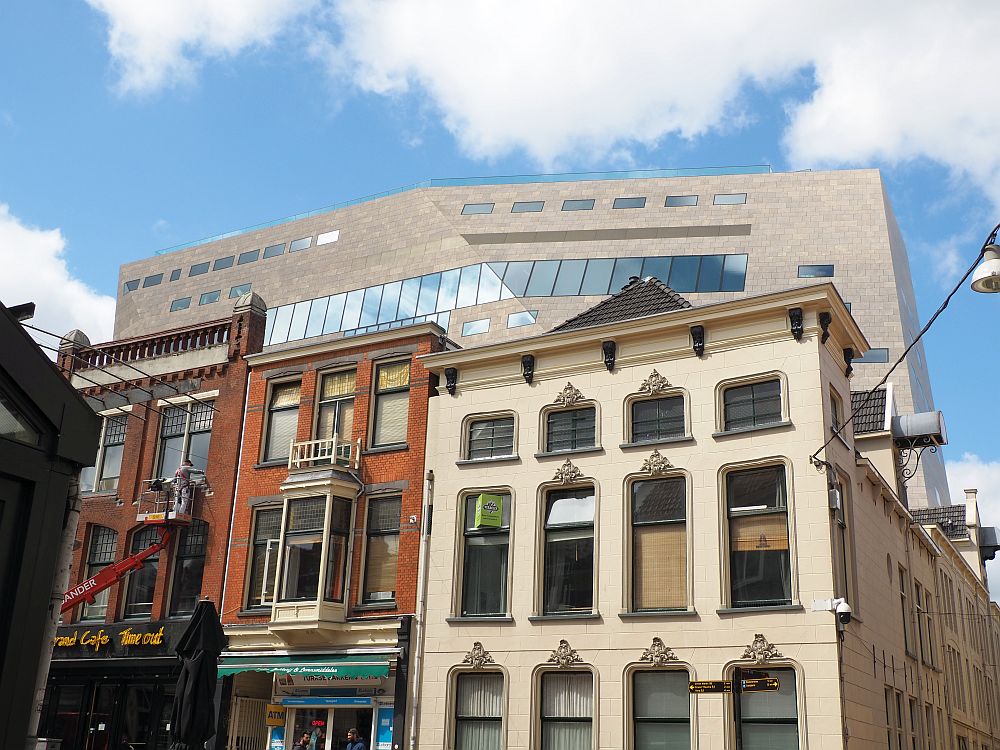 The brand-new Forum looms over a row of earlier buildings. Three buildings, each three stories in the foreground. The Forum is a block behind them, so the fact that several stories of it are visible behind all three foreground buildings shows how high and wide it is.