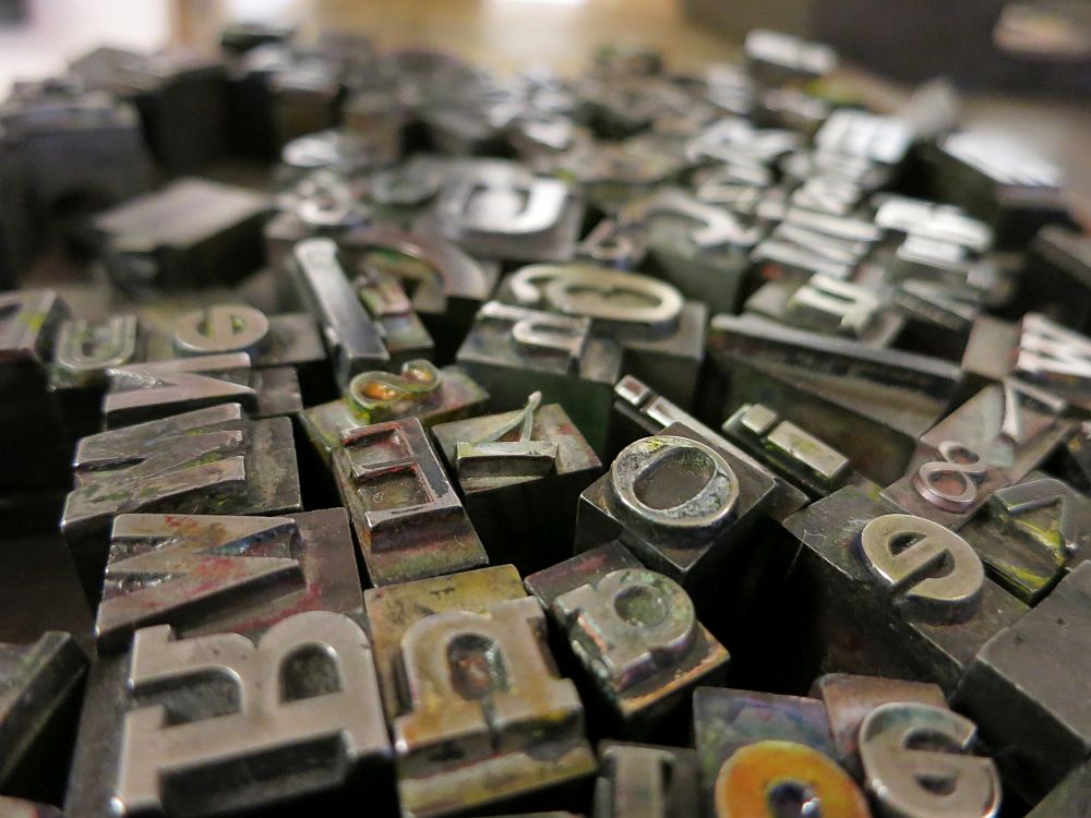 a close-up photo of a jumble of moveable type: metal squares and rectangles, each with a backward letter on it.