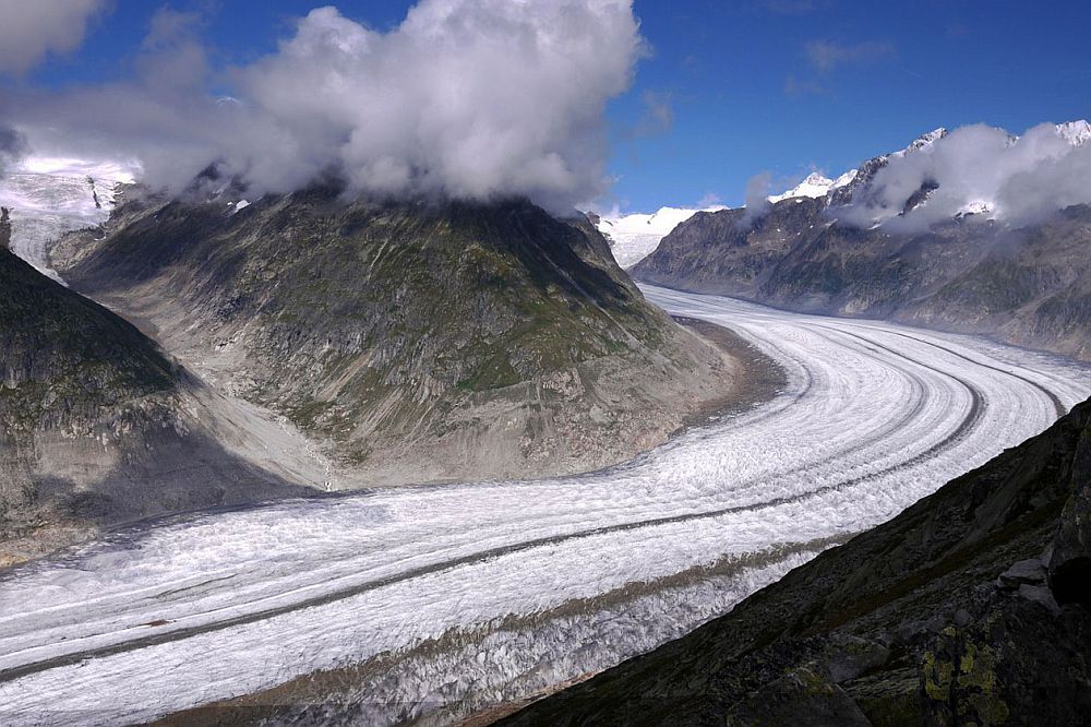 The glacier looks almost like a snow-covered road, winding from bottom left to middle right and back to the left behind a mountain. The photo looks down on the glacier, with mountains on the opposite side.